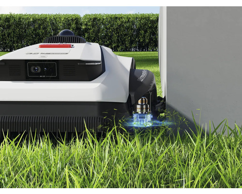 Robotgräsklippare på gräsmatta nära en vägg