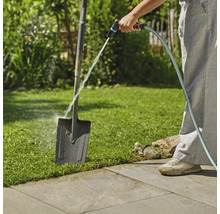 En person rengör en trädgårdsspade med en trädgårdsslang utomhus.