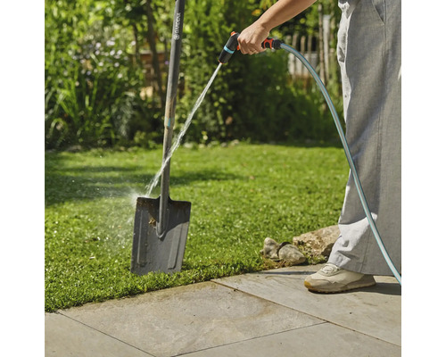 En person rengör en trädgårdsspade med en trädgårdsslang utomhus.