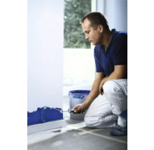 Man målar vägg med färgroller och färg från hink