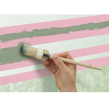 En person målar en grön linje med en rund pensel på en vägg med rosa och vita ränder