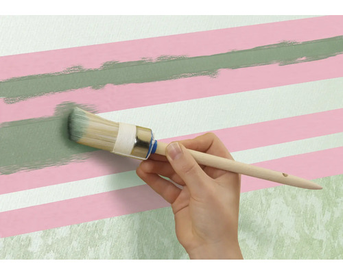 En person målar en grön linje med en rund pensel på en vägg med rosa och vita ränder