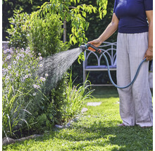 En person vattnar växter i trädgården med en trädgårdsslang.