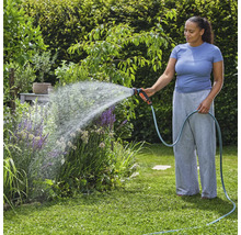 Kvinna vattnar växter med trädgårdsslang i trädgården.