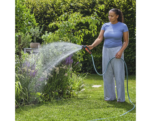Kvinna vattnar växter med trädgårdsslang i trädgården.