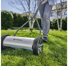 Handdriven gräsklippare med en person i trädgården.