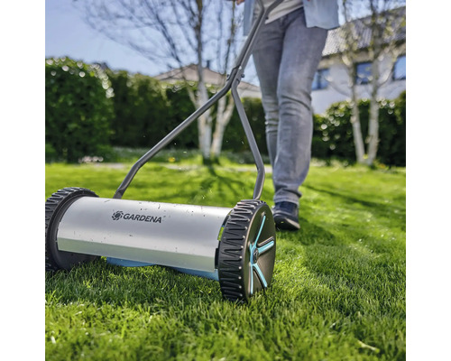 Handdriven gräsklippare med en person i trädgården.