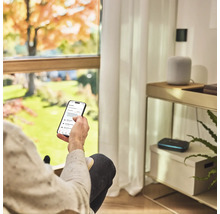 Person med smartphone för att styra trädgårdsbevattningen i vardagsrummet.