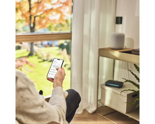 Person med smartphone för att styra trädgårdsbevattningen i vardagsrummet.