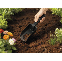 Trädgårdsspade i jorden med blommor i bakgrunden