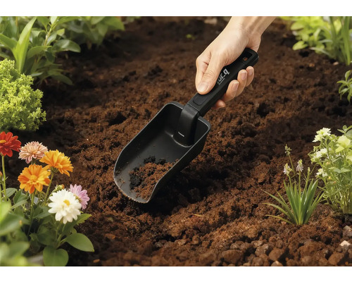 Trädgårdsspade i jorden med blommor i bakgrunden