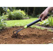 Närbild av en hand som trycker ner en trädgårdskultivator i jorden