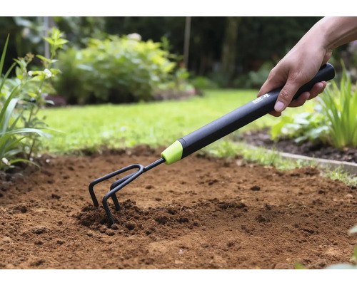 Närbild av en hand som trycker ner en trädgårdskultivator i jorden