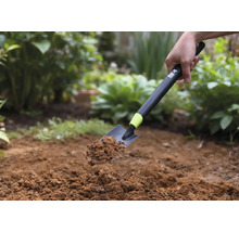 En handspade med jord hålls mot en trädgårdsbakgrund