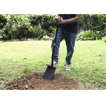 En person använder en spade i trädgården för att gräva upp jord.