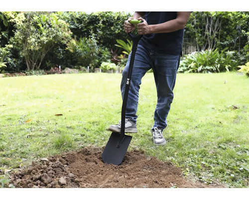 En person använder en spade i trädgården för att gräva upp jord.