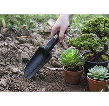 Trädgårdsspade med markeringar som används bredvid växter i krukor.