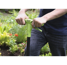 Person använder ett ogräsjärn i trädgården.