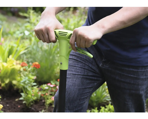 Person använder ett ogräsjärn i trädgården.