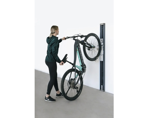 Kvinna hänger upp en elektrisk mountainbike på ett väggfäste.
