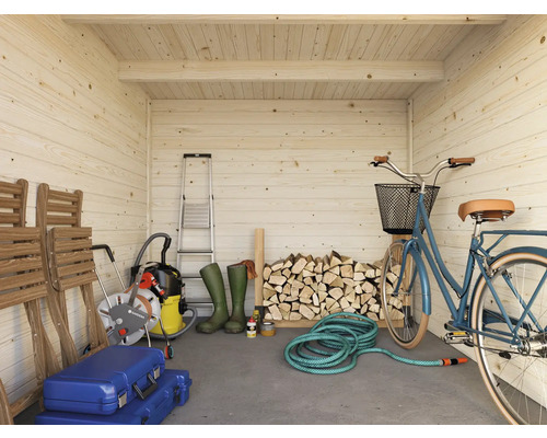 Interiör av ett ljust trädgårdshus i trä med stege, vedträn, cykel och trädgårdsredskap