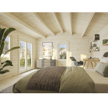 Interiörbild av ett ljust trähus med säng, skrivbord och byrå