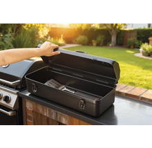 Öppen grillbesticklåda med stekspade bredvid grill i trädgården.