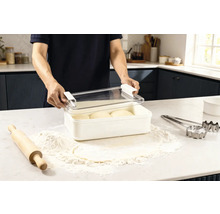 Scen i ett kök: en man öppnar en förvaringslåda med deg, omgiven av mjöl, en kavel och kakformar.