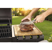 Tillagad biff skärs med en kniv på en träbräda bredvid en grill.