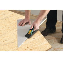 Användare bearbetar gipsskiva med kantfräs på en träskiva