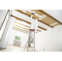 Hantverkare på en stege som utför renoveringsarbeten på ett tak i ett ljust rum.