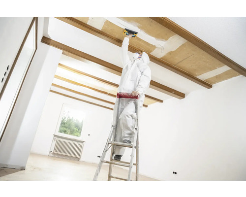 Hantverkare på en stege som utför renoveringsarbeten på ett tak i ett ljust rum.