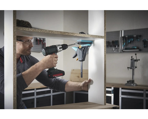 En man monterar en hylla med en sladdlös skruvdragare och en enhandsspännare.