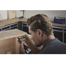 En man fäster ett gångjärn med en sladdlös skruvdragare på ett träskåp.