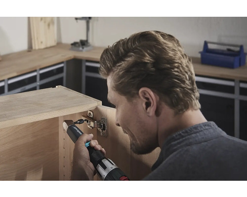 En man fäster ett gångjärn med en sladdlös skruvdragare på ett träskåp.