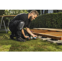 En man bygger en träterrass med en sladdlös skruvdragare och knäskydd i trädgården.