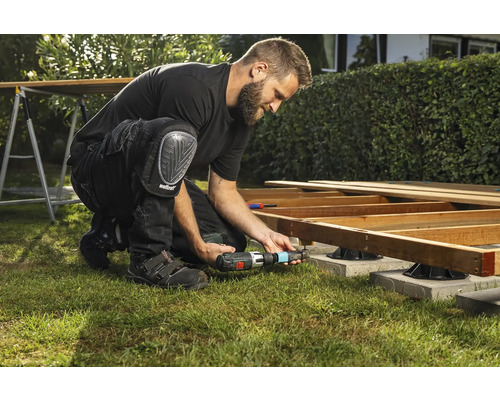 En man bygger en träterrass med en sladdlös skruvdragare och knäskydd i trädgården.