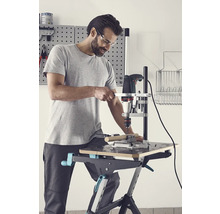 Man borrar ett arbetsstycke med en borrmaskin och ett borrstativ på en arbetsbänk.