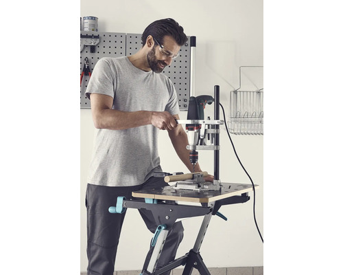 Man borrar ett arbetsstycke med en borrmaskin och ett borrstativ på en arbetsbänk.