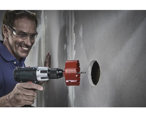 En man med skyddsglasögon borrar ett hål i en vägg med en hålsåg.