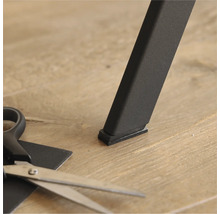 Möbelglid under ett bordsben och en sax för att klippa till rätt storlek