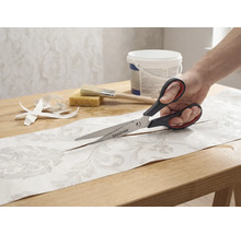 En person klipper en bit mönstrad tapet med en Rautner-sax på ett bord