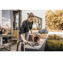 Kvinna rengör terrassen med dammsugare bredvid blomkruka