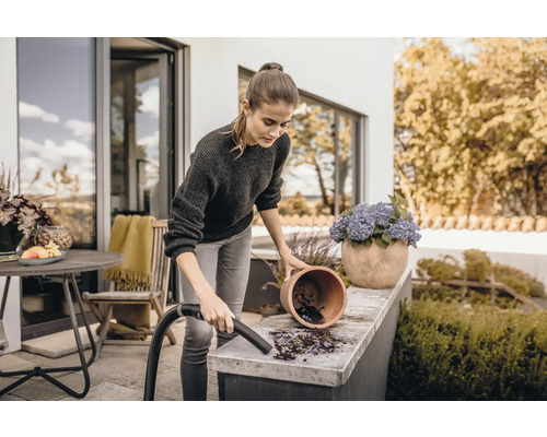 Kvinna rengör terrassen med dammsugare bredvid blomkruka