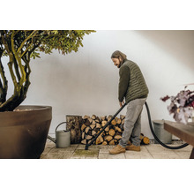 Man rengör terrassen med en askdammsugare, med en vedstapel och en växt i bakgrunden