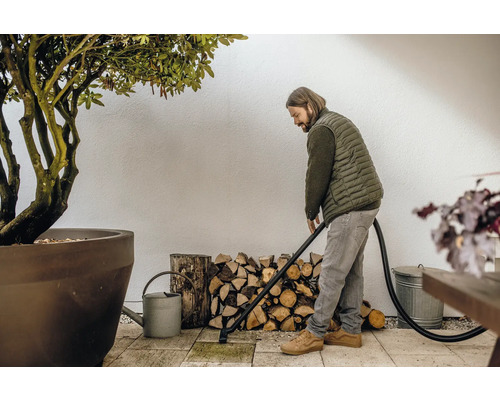 Man rengör terrassen med en askdammsugare, med en vedstapel och en växt i bakgrunden