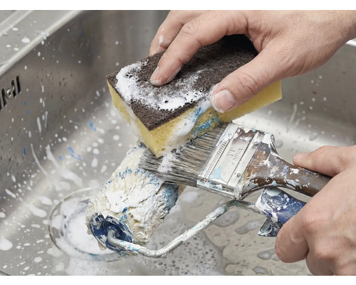 Rengöring av färgrulle och pensel med en svamp i diskhon.