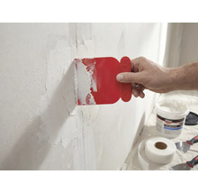 En man applicerar en röd spackel på en vägg med glasfibertejp