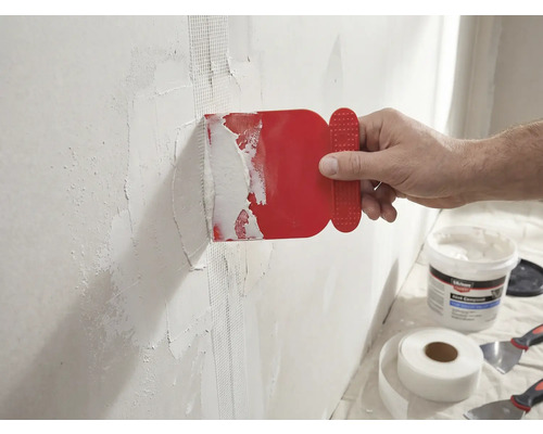 En man applicerar en röd spackel på en vägg med glasfibertejp