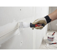 Hantverkare spacklar väggen med spackel och spackel. Rautner Logo syns.